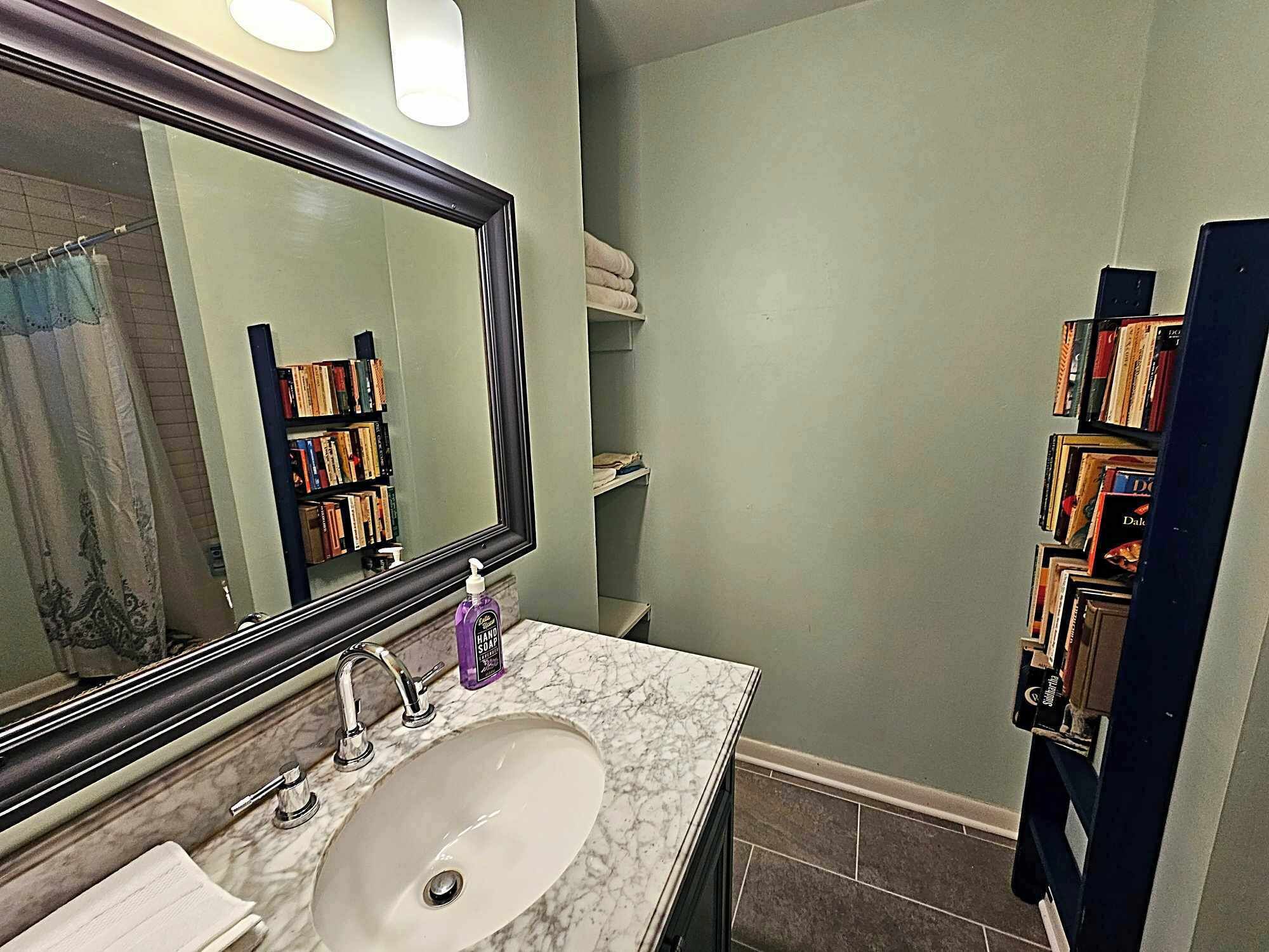 A bathroom with a marble sink, a large mirror, and a shelf with toiletries.