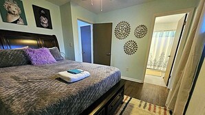 A bedroom with a large bed, a door leading to another room, and a wall with decorative circular patterns. - The Castro (Dayton)