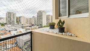 A balcony with a view of a cityscape, featuring a chain-link fence, potted plants, and a window. - Studio With Balcony Sp-an606 (São Paulo)