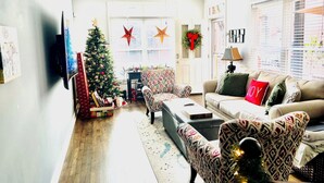 A living room with a Christmas tree, patterned armchairs, a sofa with a 'JOY' pillow, and a ceiling fan. - Cozy 2-bedroom Townhome with free parking in charming Downtown Chattanooga (Chattanooga)