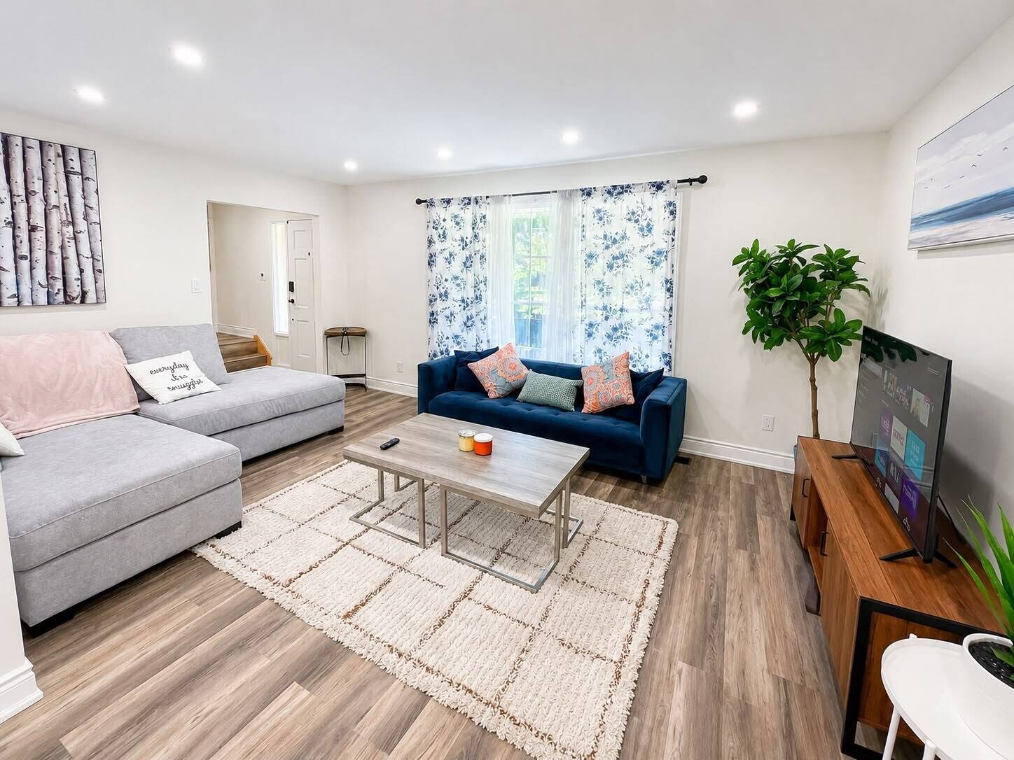 Un salon moderne avec un canapé gris, un canapé bleu, une table basse et un téléviseur posé sur un meuble en bois.