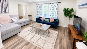 Ein modernes Wohnzimmer mit einem grauen Sofa, einem blauen Sofa, einem Couchtisch und einem Fernseher auf einem Holzgestell.
