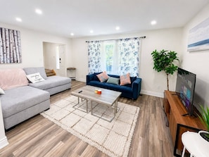 Una sala moderna con un sofá gris, un sofá azul, una mesa de centro y un televisor sobre un mueble de madera.