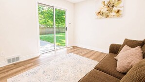 Ein Wohnzimmer mit einem braunen Sofa, einem gemusterten Teppich und einer Schiebetür, die in einen Garten führt.