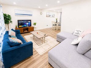 A modern living room with a blue sofa, a grey sofa, a wooden coffee table, and a TV on a wooden stand.