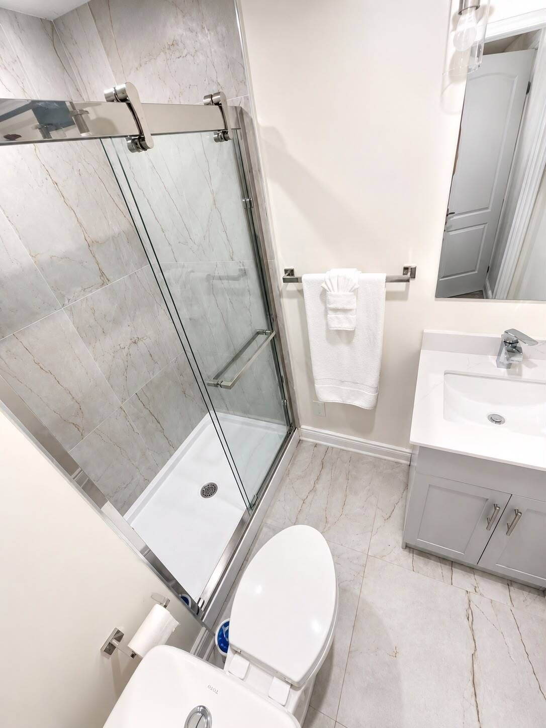 A modern bathroom with a glass shower enclosure, a white toilet, a sink with a mirror, and a towel rack.