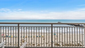 Une vue sur la plage depuis un balcon doté d’une balustrade, avec les vagues de l’océan et des parasols de plage.