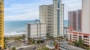 Un grand hôtel à plusieurs étages, avec vue sur la plage et un parking où sont garées des voitures.