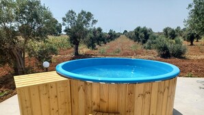Ein hölzerner Whirlpool mit blauer Innenauskleidung, umgeben von einer Holzterrasse und Stufen, eingebettet in einen angelegten Garten mit Bäumen und Sträuchern.
