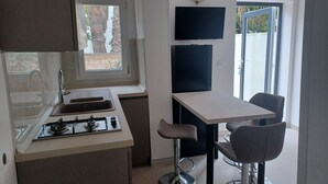 Eine kleine Küche mit Gaskochfeld, Spüle und Fenster mit Blick auf einen Garten.