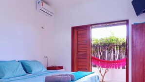 A bedroom with a bed, a wooden door, a hammock, and a small table with glasses. - Charming bungalow in garden with lot of privacy - in an exclusive condo. (Guajiru Trairi)