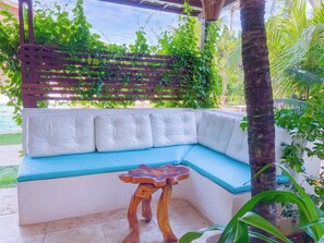 A covered outdoor seating area with a cushioned bench and a wooden table.