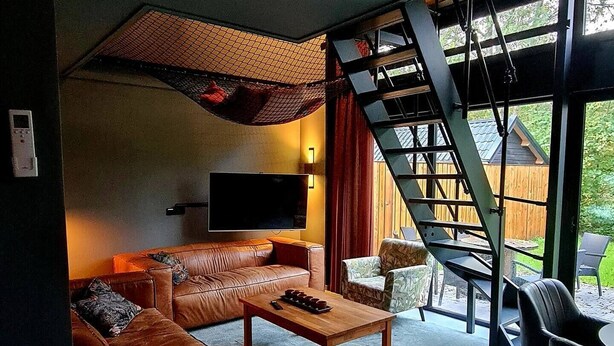 A modern living room with a large brown leather sofa, a flat-screen TV, and a staircase leading to an outdoor area. - Charming 3-bedroom house in enchanting Ternaard with WiFi, AC "Us Eigen Honk" (Ternaard)
