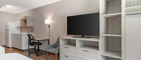 Una habitación de hotel moderna con una cama, un escritorio con una silla, un televisor y un armario.