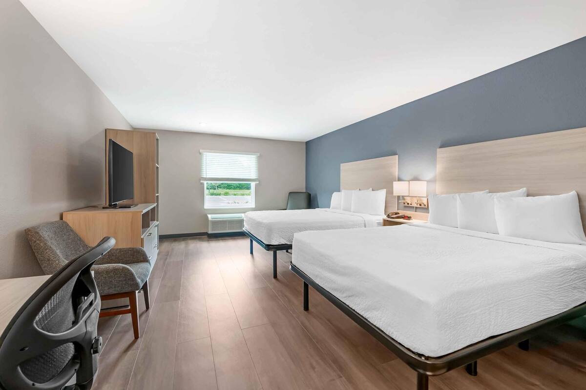 A hotel room with two beds, a desk, a chair, a TV, and a window with blinds.