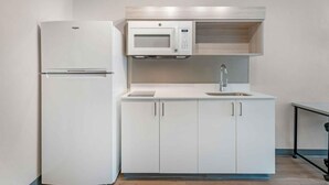 Een kleine keuken met een ingebouwde koelkast, een magnetron, een spoelbak en keukenkastjes.