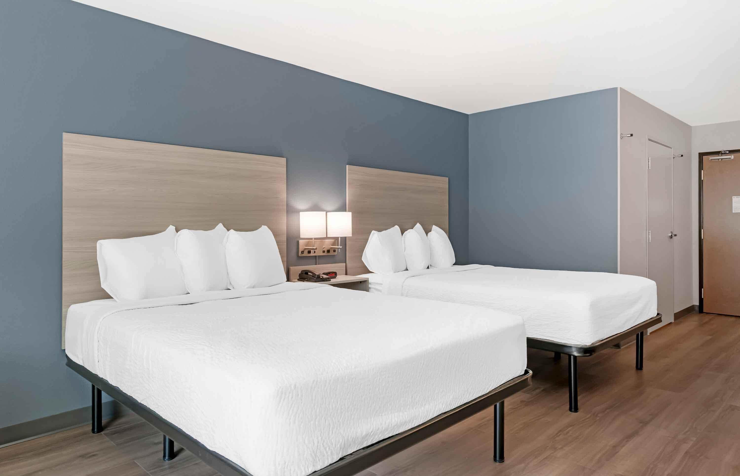 A hotel room with two beds, a nightstand with a lamp, and a wardrobe.