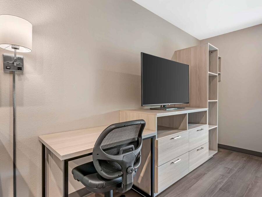 Quarto moderno com televisão de tela plana, escrivaninha, cadeira e prateleiras embutidas.