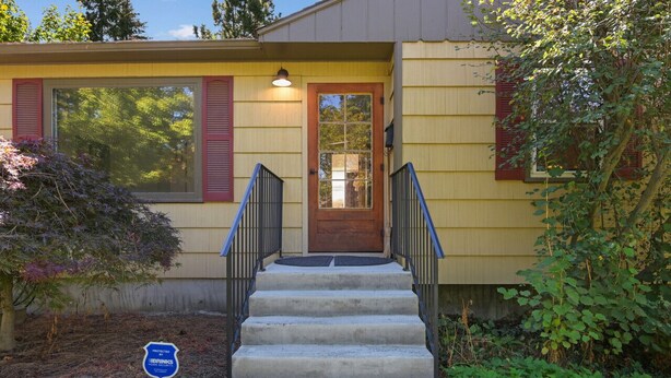 A house with a front porch, a set of concrete stairs leading to the door, and a small garden area with a sign indicating a protected drinking water source. - The Canon Hill Cottage (Spokane)