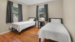 A room with two single beds, a small table with a lamp, and a window with curtains. - The Canon Hill Cottage (Spokane)
