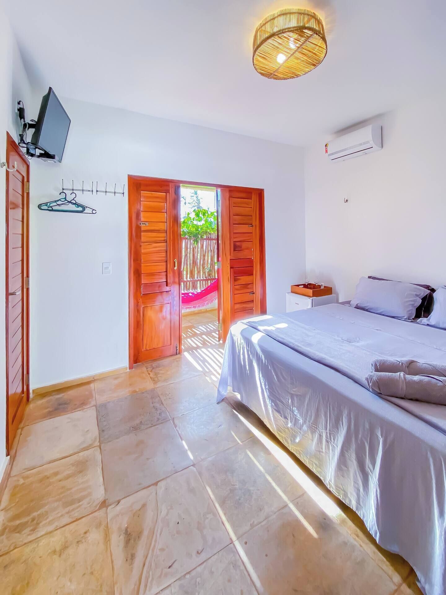 Quarto com cama, televisão, porta de madeira e vista para o exterior.