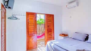 Een slaapkamer met een bed, een televisie, een houten deur en uitzicht op buiten.