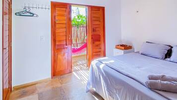 Quarto com cama, televisão, porta de madeira e vista para o exterior.