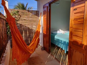 Una habitació amb un llit, un hamaca i una porta de fusta.