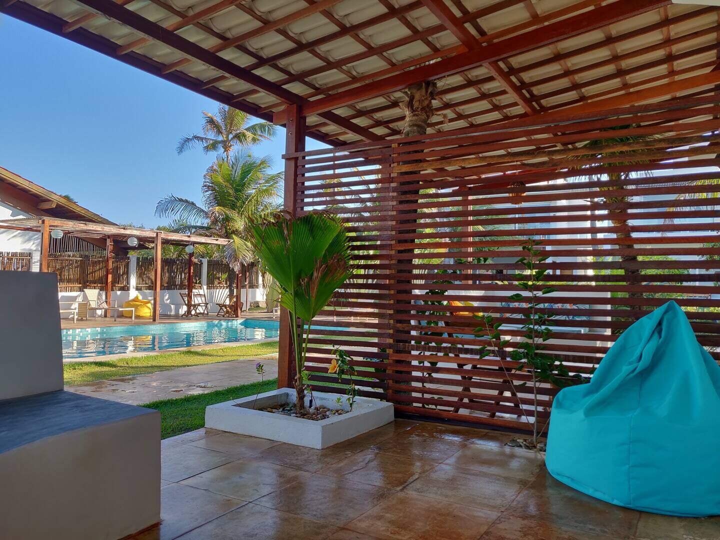 Área externa coberta com piscina, paredes de ripas de madeira e um assento de poliestireno azul.