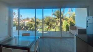 Un'ampia stanza con un'ampia porta scorrevole in vetro che dà su un balcone con vista su palme e cielo sereno.