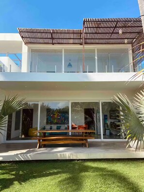 Une maison moderne à deux étages, dotée d’un patio couvert, de grandes fenêtres et d’une pelouse verdoyante.