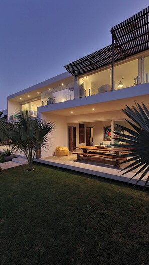 Une maison moderne à deux étages, dotée d’un toit plat, de grandes fenêtres et d’un patio couvert.