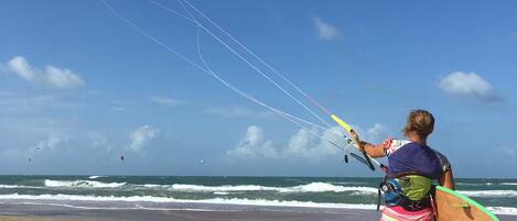 Une personne se promène sur une plage de sable, tenant un cerf-volant et une planche de surf.