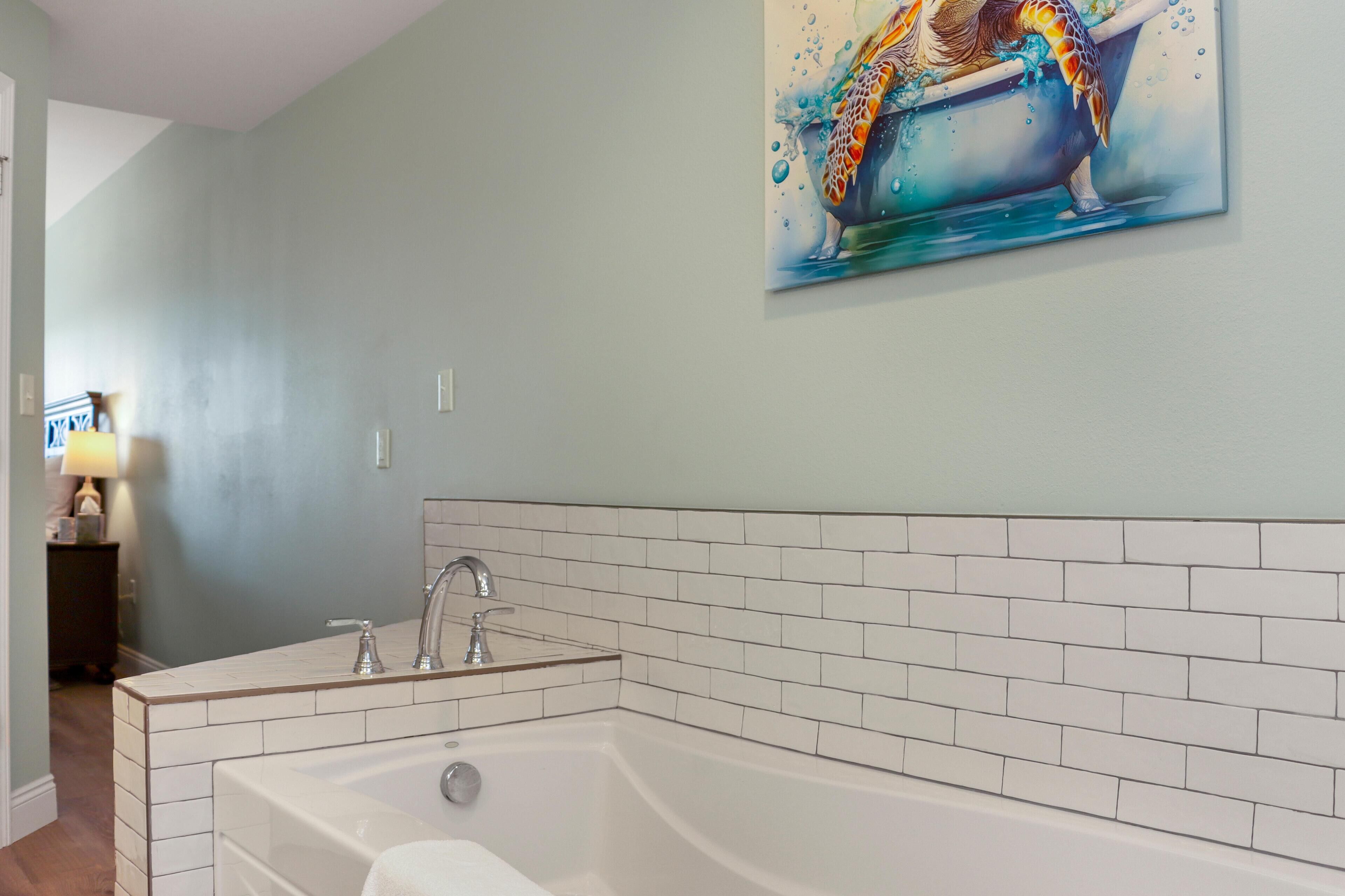 A bathroom with a large bathtub, white subway tiles, and a painting of a turtle on the wall.