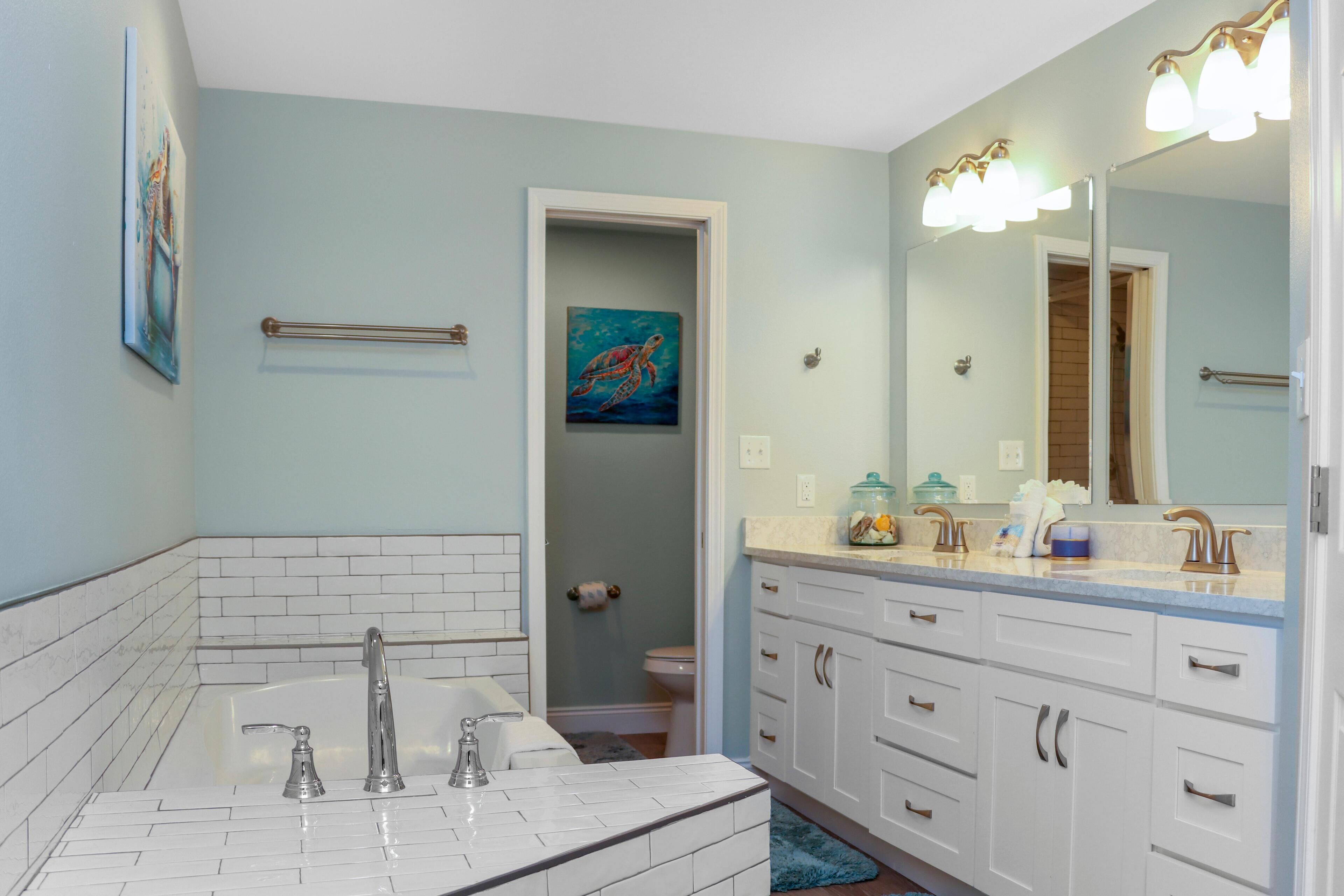 Une salle de bain avec une baignoire, un lavabo et un meuble-lavabo avec des tiroirs. Il y a un tableau au mur et un miroir au-dessus du lavabo.