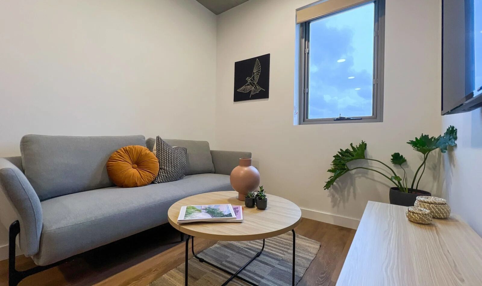 A modern living room with a grey sofa, a round coffee table, a vase, and potted plants.