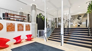 Een moderne lobby met een trap, rode stoelen en kunstwerken aan de muren.