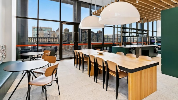 Een moderne eetruimte met grote ramen, een lange houten tafel en meerdere stoelen.