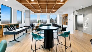 Een moderne lounge met een pooltafel, barstoelen en grote ramen met uitzicht op de stad.