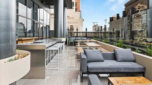 Een dakterras met een modern design, voorzien van een bank, barstoelen en een lange bar.