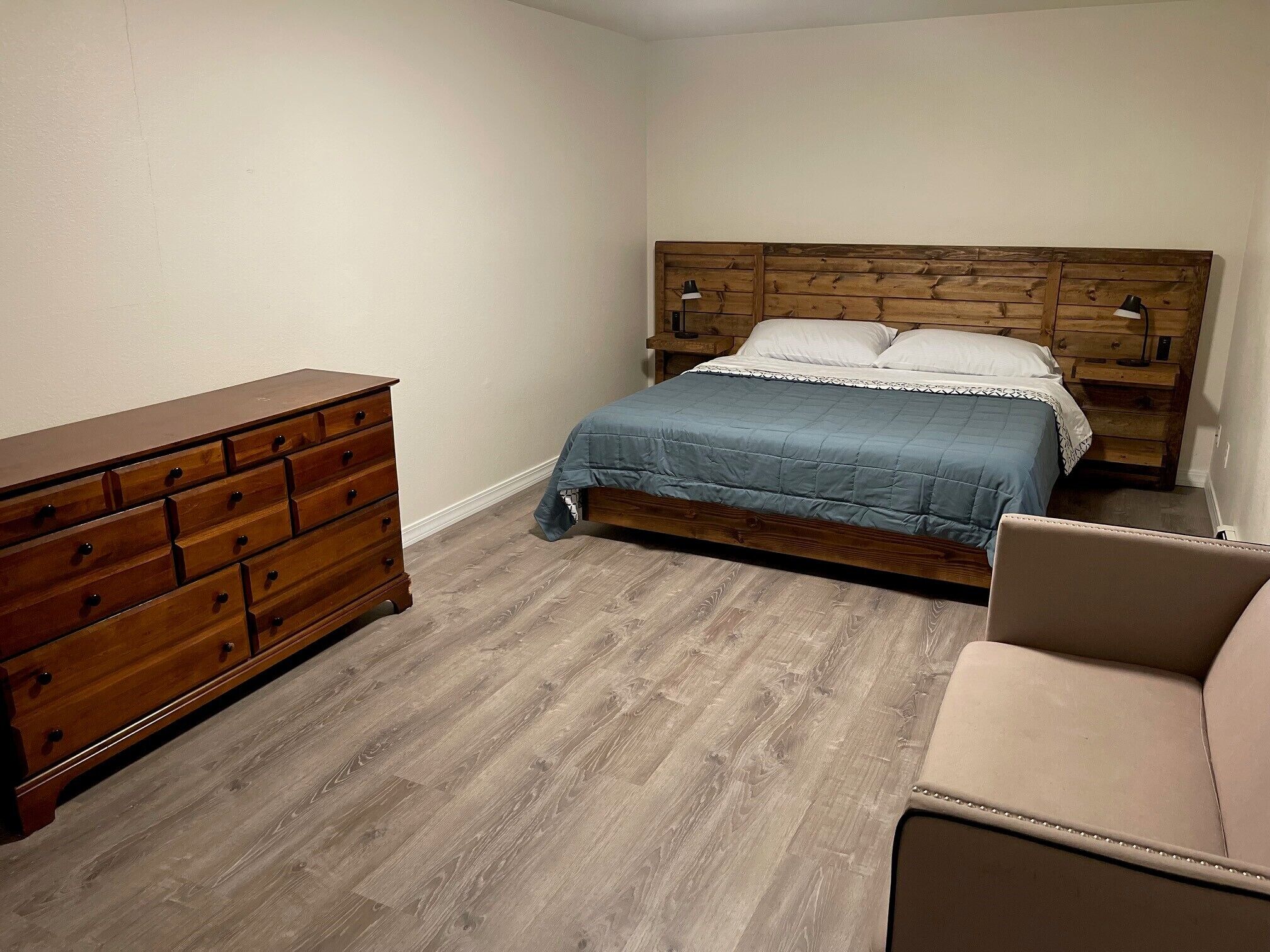 Ein Schlafzimmer mit einem hölzernen Schminktisch, einem Bett mit blauer Bettdecke und einem Nachttisch mit Lampe.