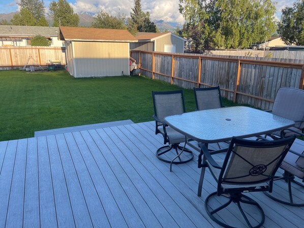 A deck with a table and chairs, surrounded by a wooden fence and a grassy yard.