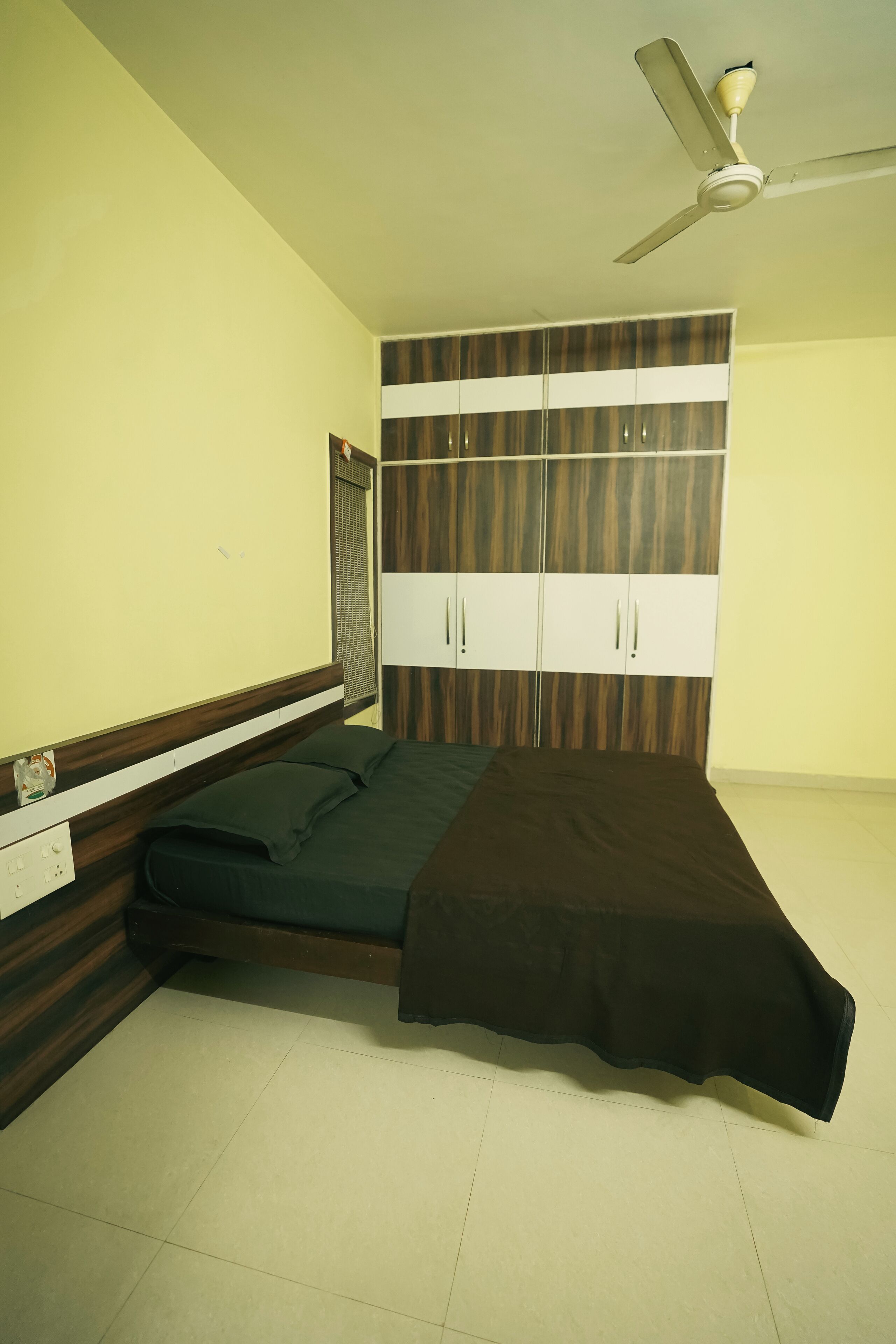 Une chambre à coucher comprenant un lit, une armoire, un ventilateur de plafond et une fenêtre avec des stores.