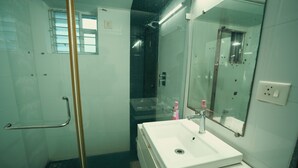 Un baño con cabina de ducha de vidrio, un lavabo blanco con espejo y dispensador de gel hidroalcohólico.