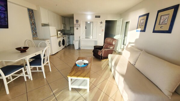 Un espacio habitable compacto con comedor, sofá, mesa de centro y zona de cocina que incluye lavadora.