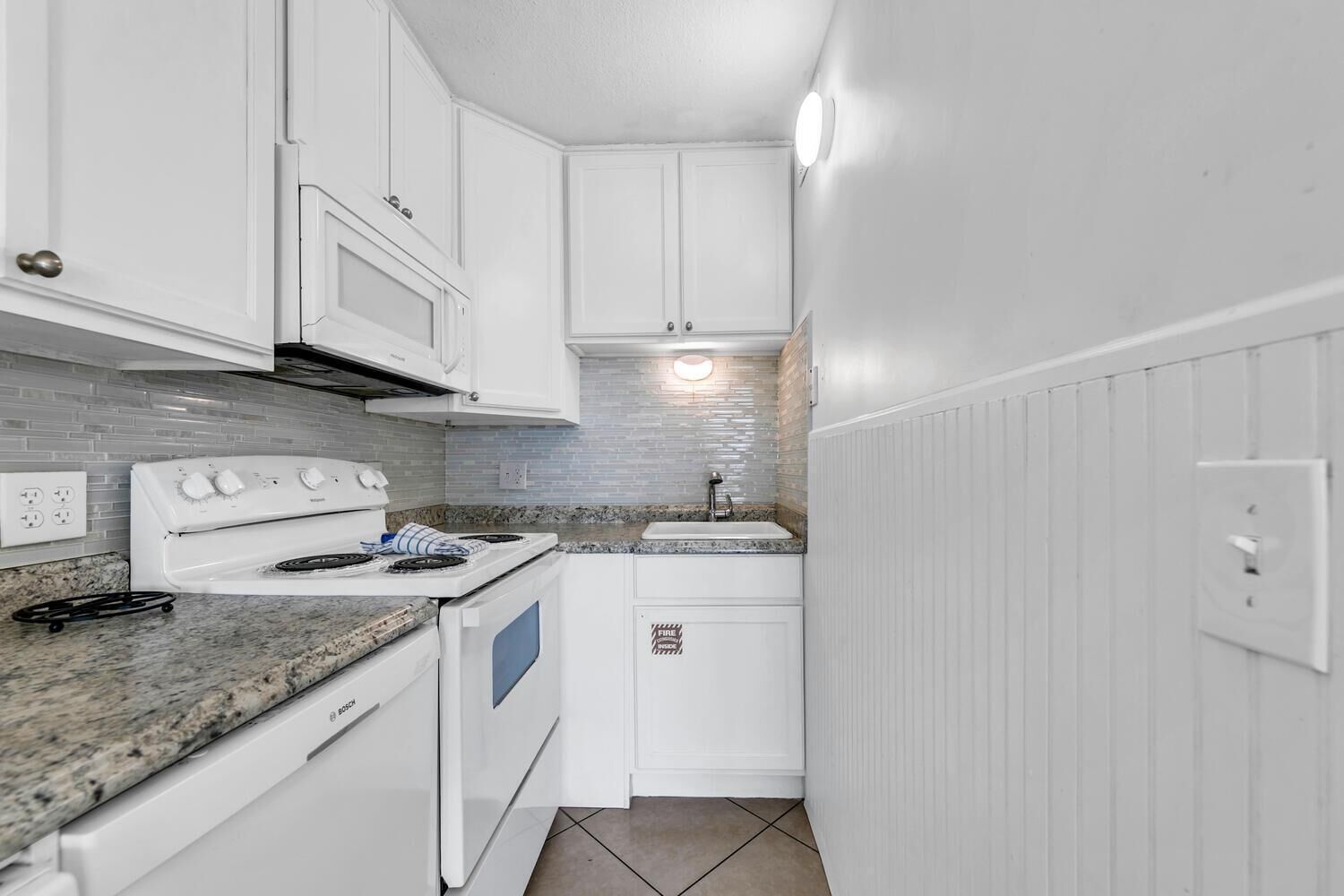 A compact kitchen with white cabinets, a Bosch oven, a stove, and a sink.
