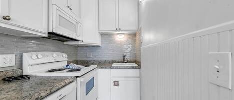 A compact kitchen with white cabinets, a Bosch oven, a stove, and a sink.