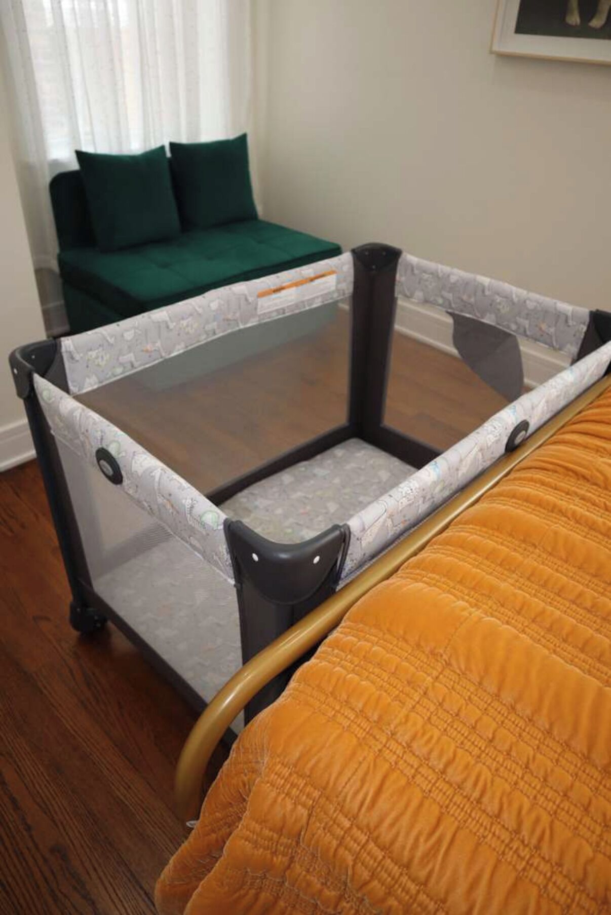 Et værelse med en seng, en grøn sofa og en rejseseng til baby.