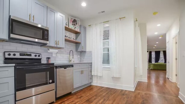 A modern kitchen with stainless steel appliances, white cabinetry, and a wooden floor. - Modern Cozy Apartment, Free Parking, Wi-Fi, Near Dining and Downtown. (Chicago)