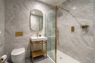 Un baño moderno con ducha de vidrio, tocador con marco dorado y pared cubierta de mármol.